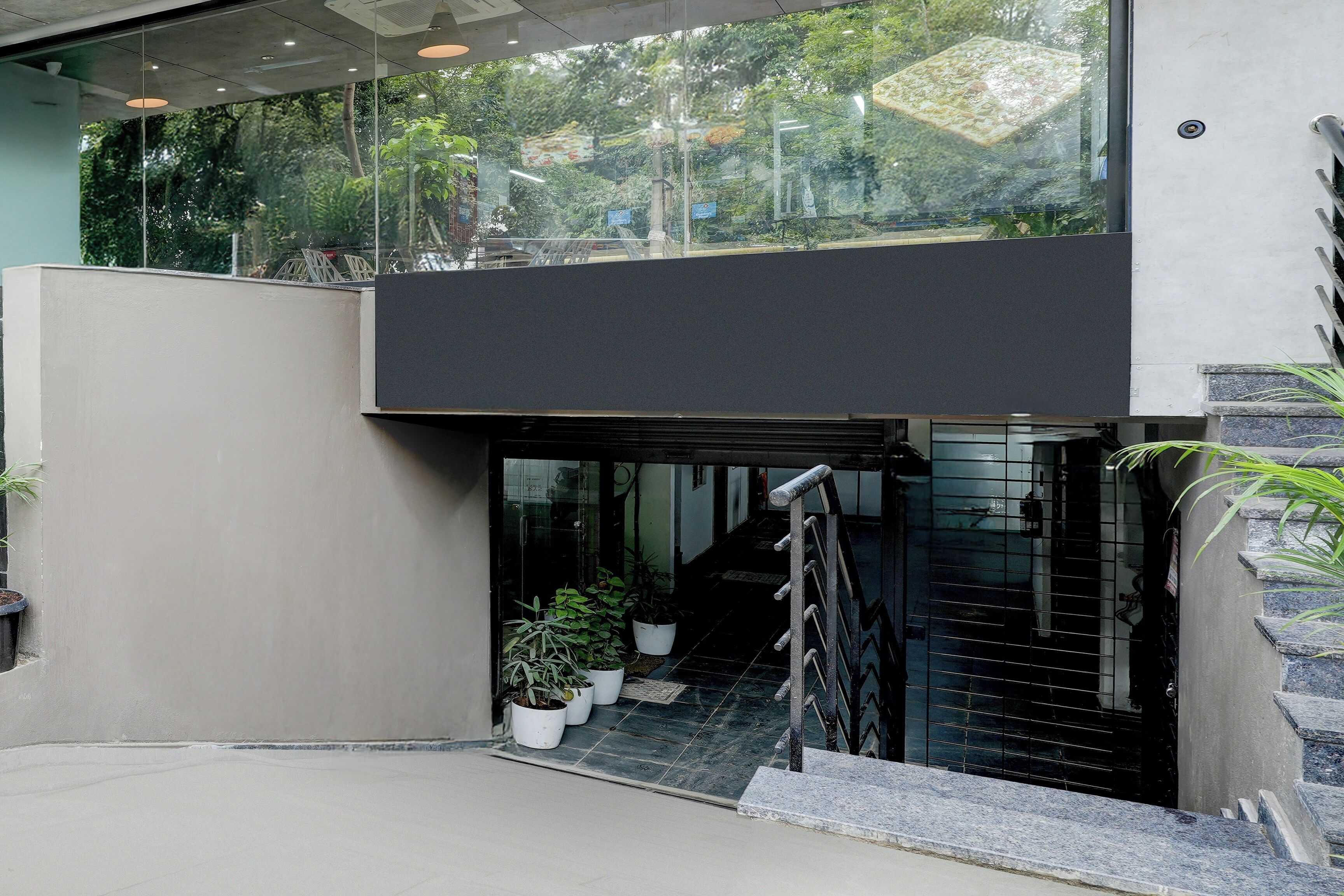 A modern building entrance with a glass door, potted plants, and a metal staircase.