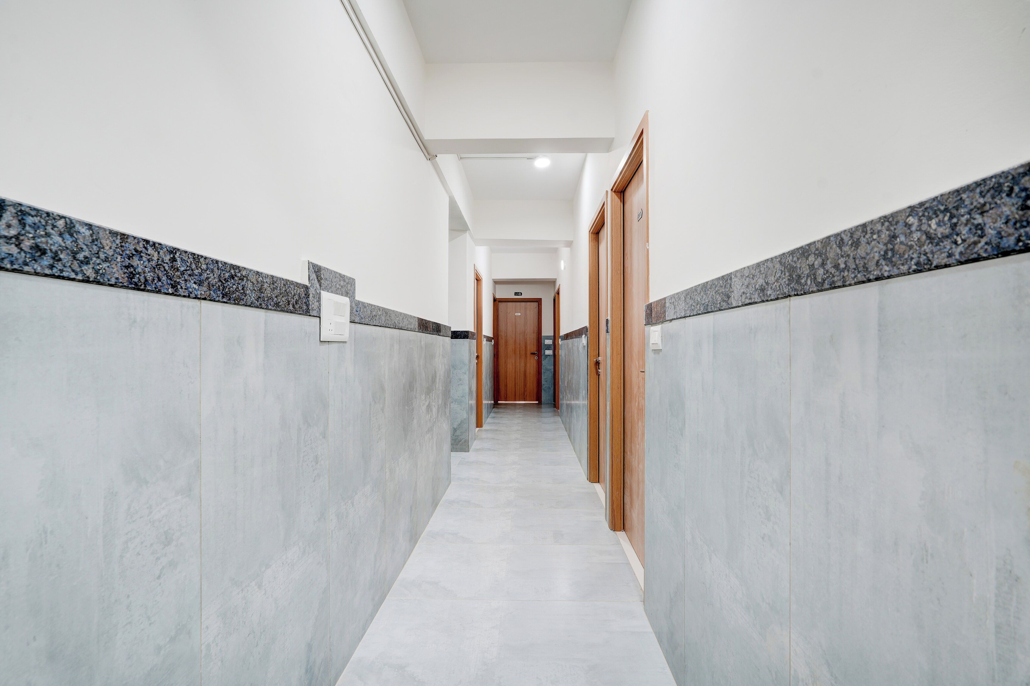 A hallway with a marble floor and walls, leading to a wooden door at the end.
