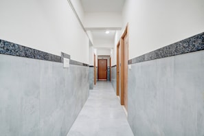 A hallway with a marble floor and walls, leading to a wooden door at the end. - Hotel O by OYO Arrow Inn (Bangalore)