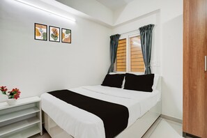 A bedroom with a bed, a nightstand, a vase with flowers, and three wall-mounted pictures. - Hotel O by OYO Arrow Inn (Bangalore)