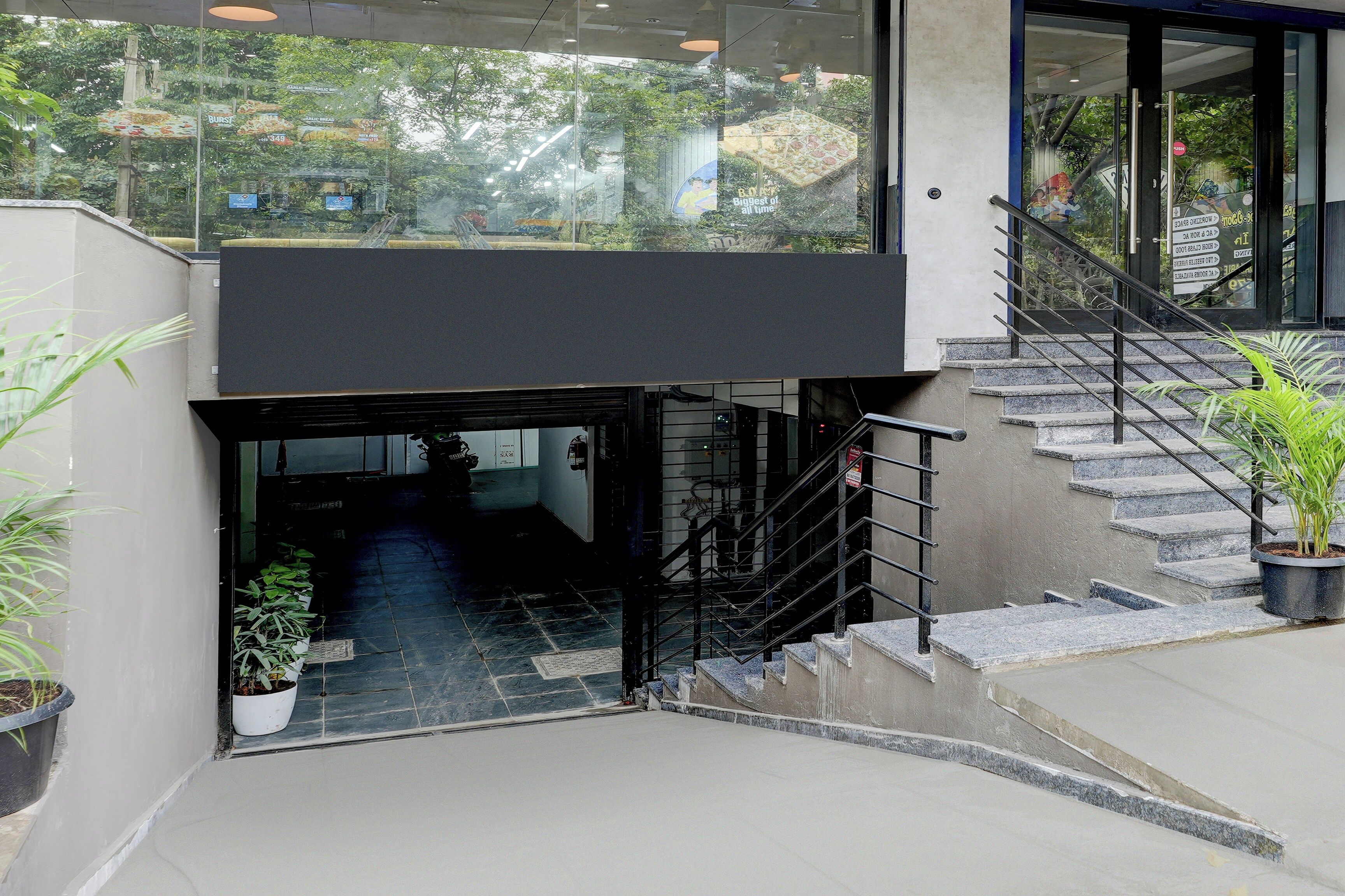 A modern building entrance with a glass door, a staircase, and potted plants.