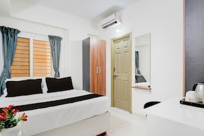 A hotel room with a bed, a desk with a chair, a wardrobe, a door, and an air conditioning unit. - Hotel O by OYO Arrow Inn (Bangalore)