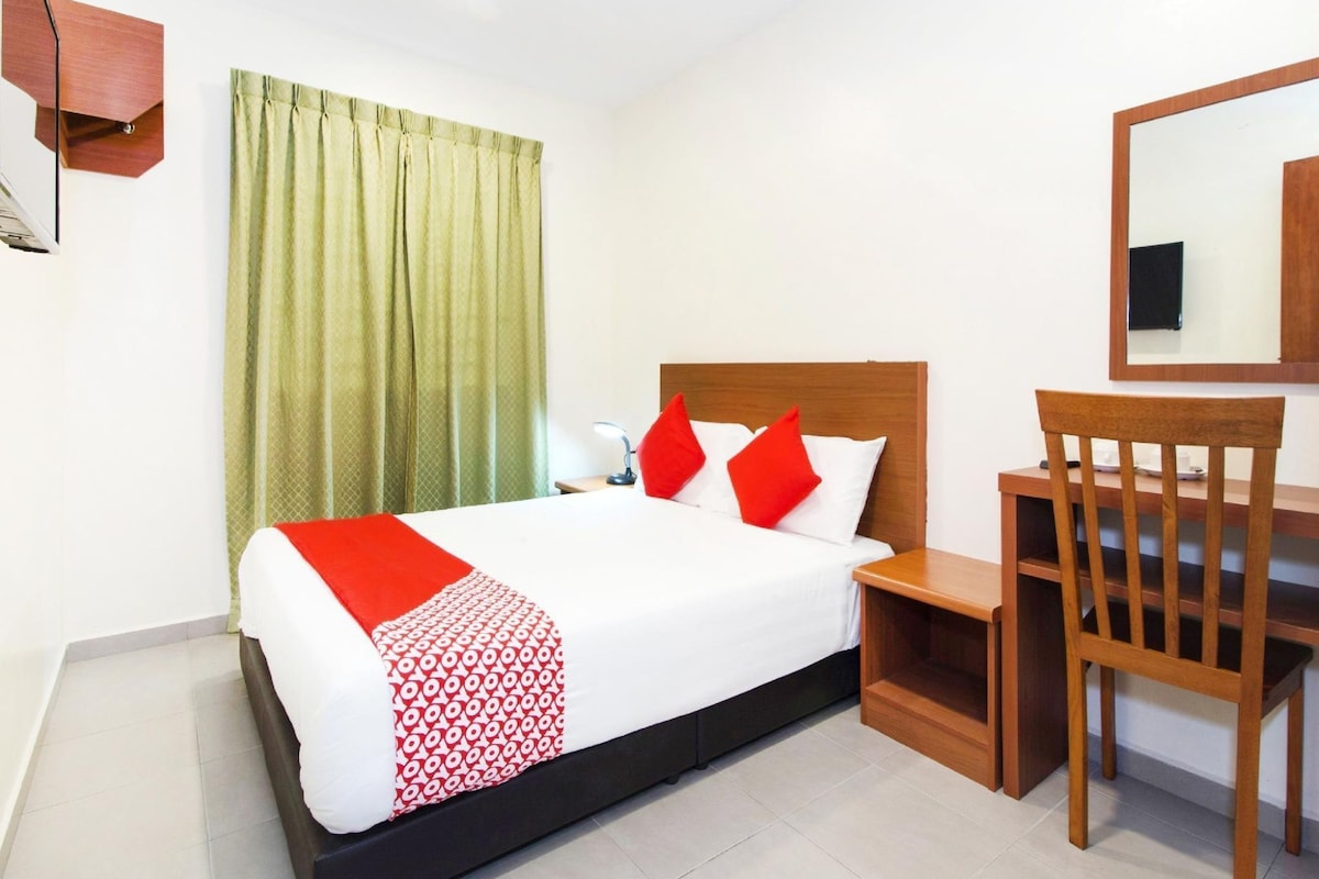 A hotel room with a bed, a desk, a chair, a mirror, and a window with curtains.