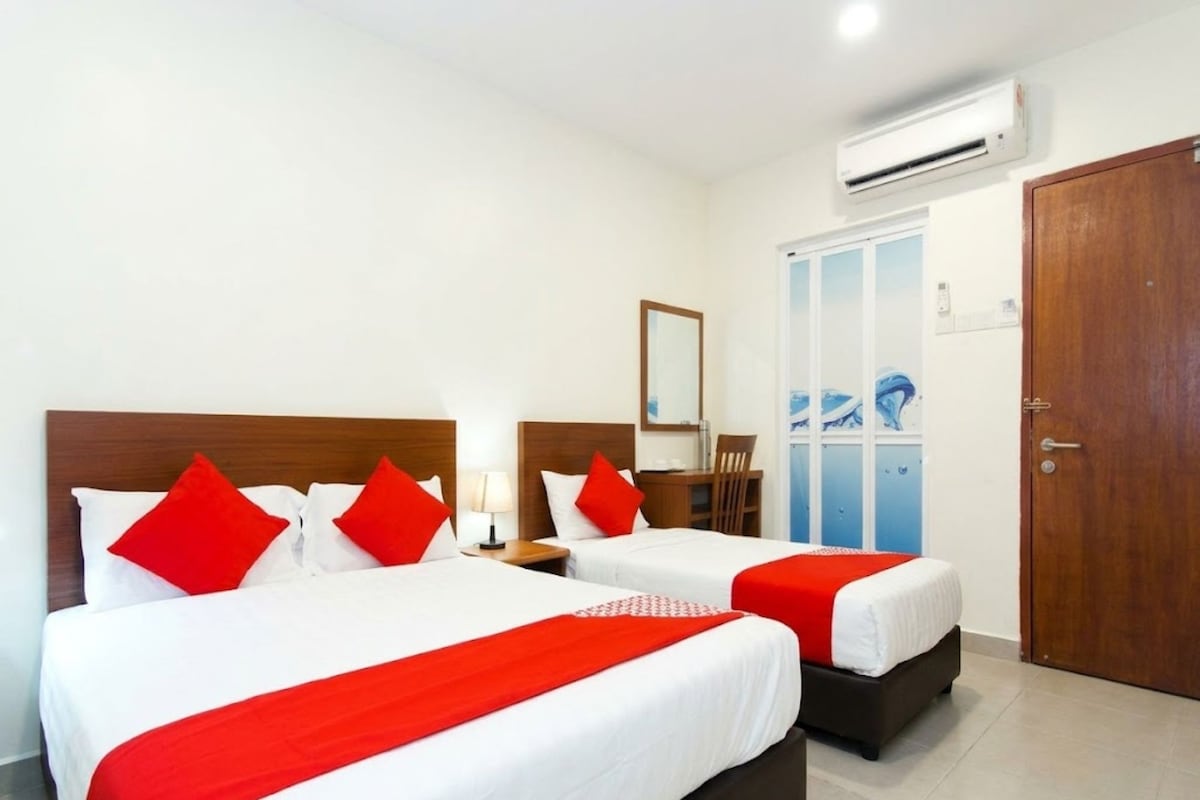 A hotel room with two beds, each with red and white bedding, a wooden headboard, a nightstand, a mirror, and an air conditioning unit.