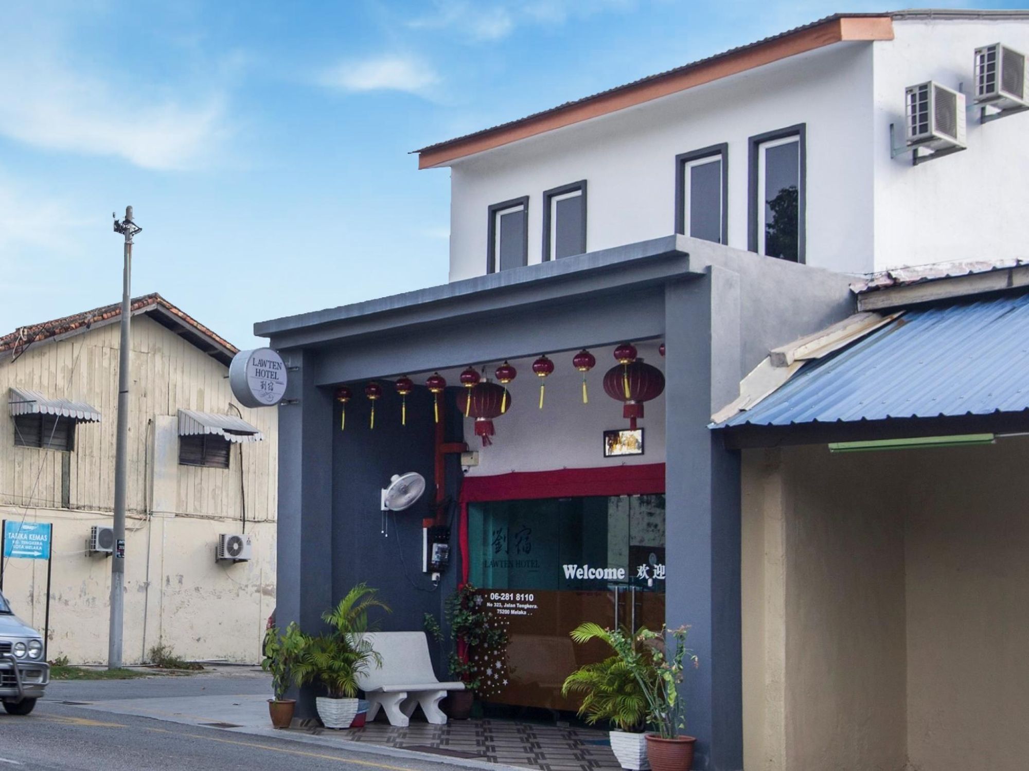 A hotel with a red and white facade, a welcoming sign, and potted plants in front.