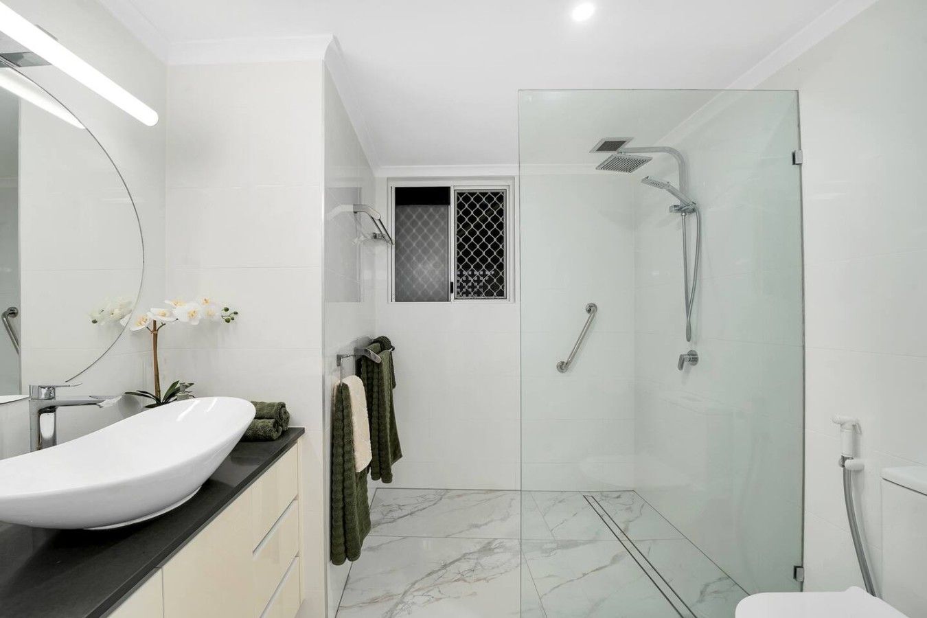 A modern bathroom with a glass-enclosed shower, a white sink, and a mirror.