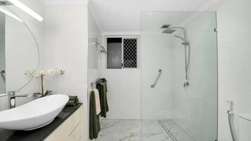 A modern bathroom with a glass-enclosed shower, a white sink, and a mirror.