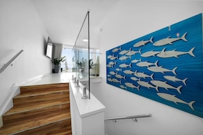 Een modern interieur met een trap, blauwe muurkunst van vissen en een glazen balustrade.