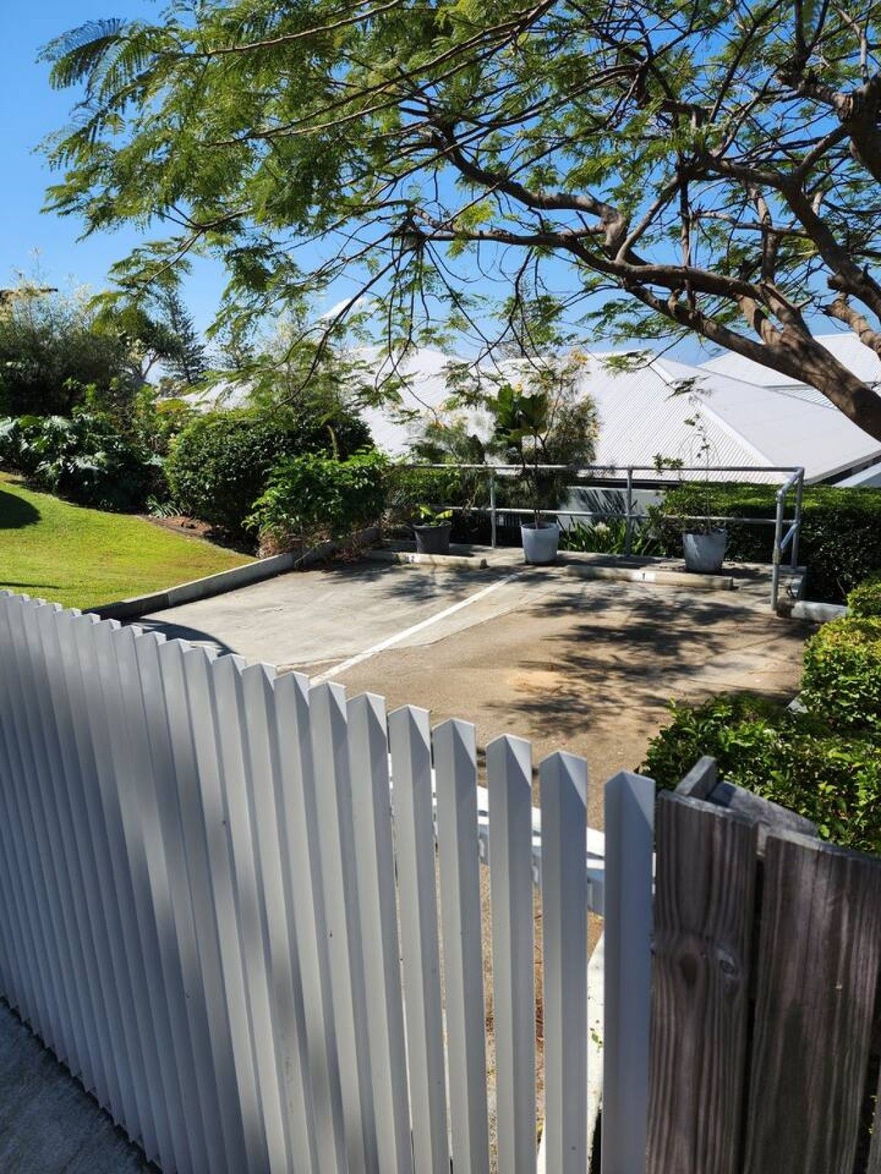 A fenced outdoor area with a paved surface, surrounded by greenery and trees.