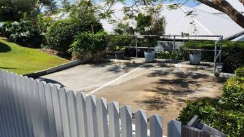 A fenced outdoor area with a paved surface, surrounded by greenery and trees.