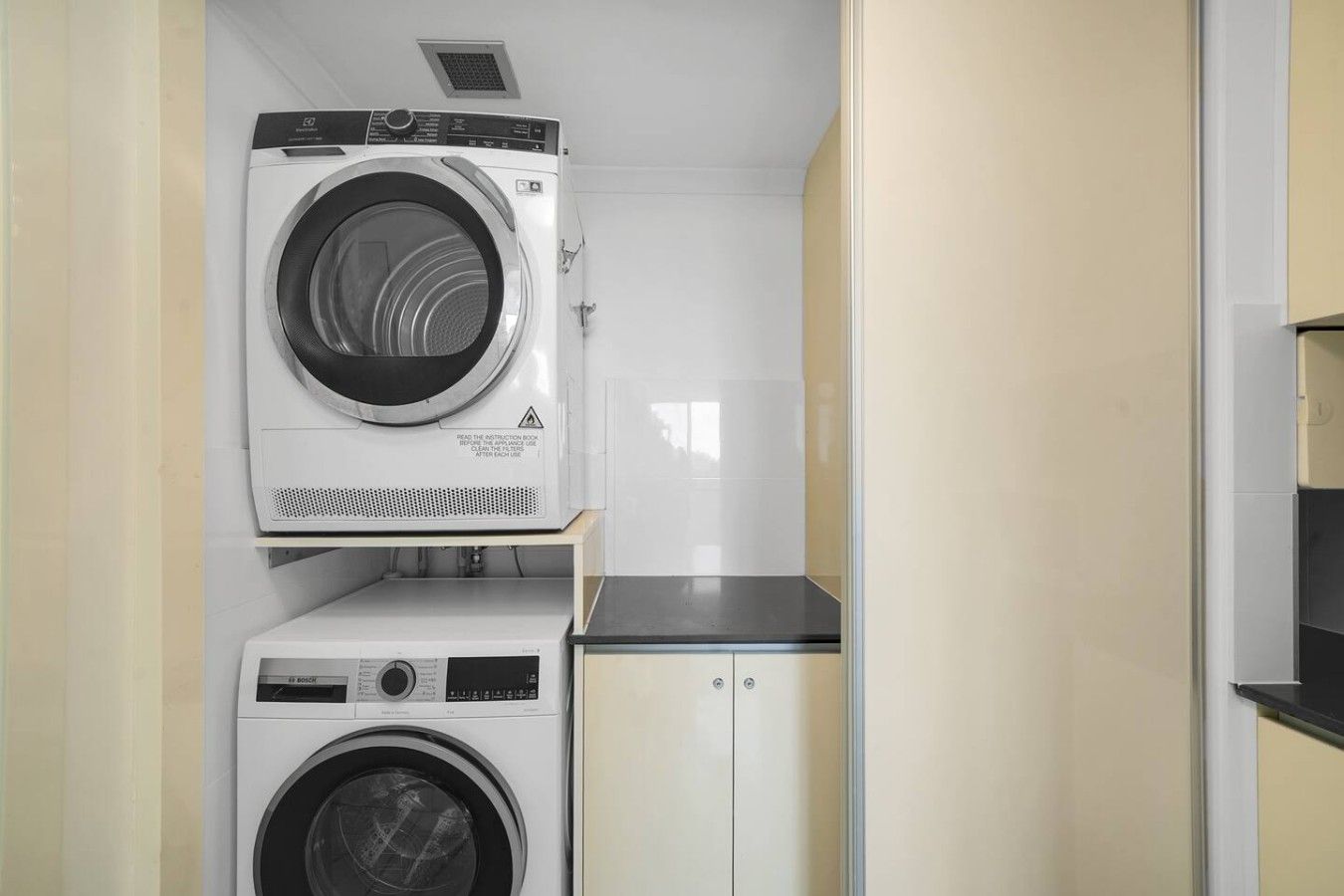 A compact laundry room with two stacked washing machines, a small countertop, and a cabinet.