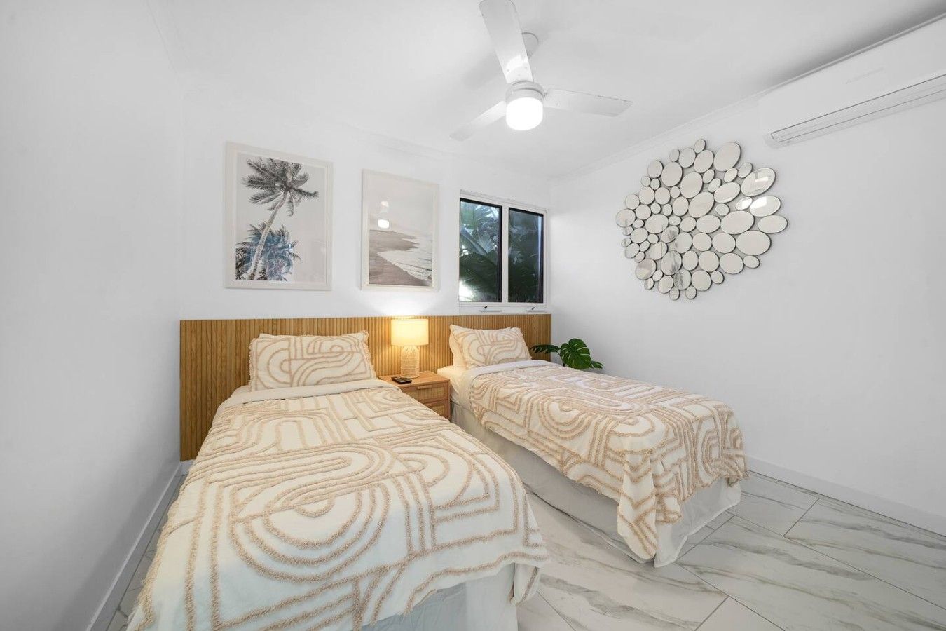 A bedroom with two beds, a ceiling fan, wall-mounted artwork, and a circular mirror decoration.