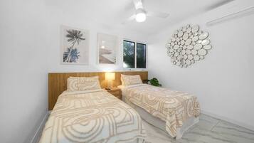 A bedroom with two beds, a ceiling fan, wall-mounted artwork, and a circular mirror decoration.