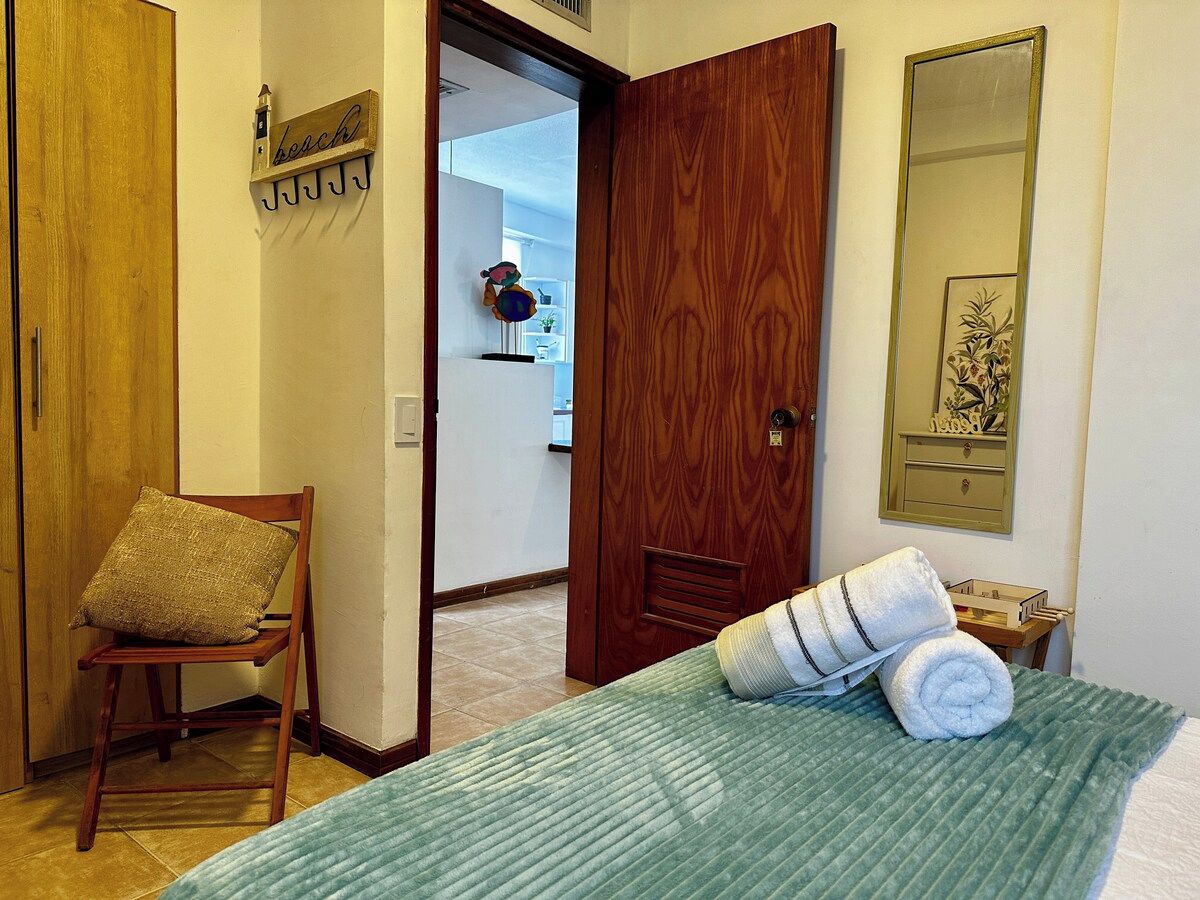 Une chambre d’hôtel avec un lit, une chaise, une porte en bois et un porte-serviettes fixé au mur.