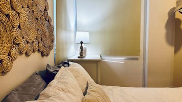 A bedroom with a bed, pillows, a nightstand with a lamp, and a wall with woven decorations.