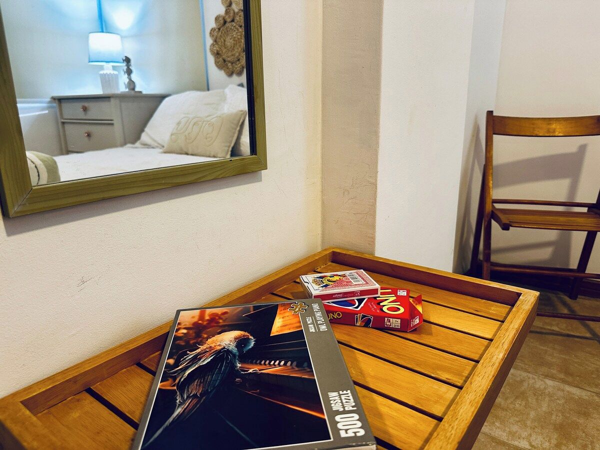 Uma mesa de madeira com uma caixa de quebra-cabeça e uma caixa de chocolates LINO. Uma cadeira de madeira fica ao lado da mesa.