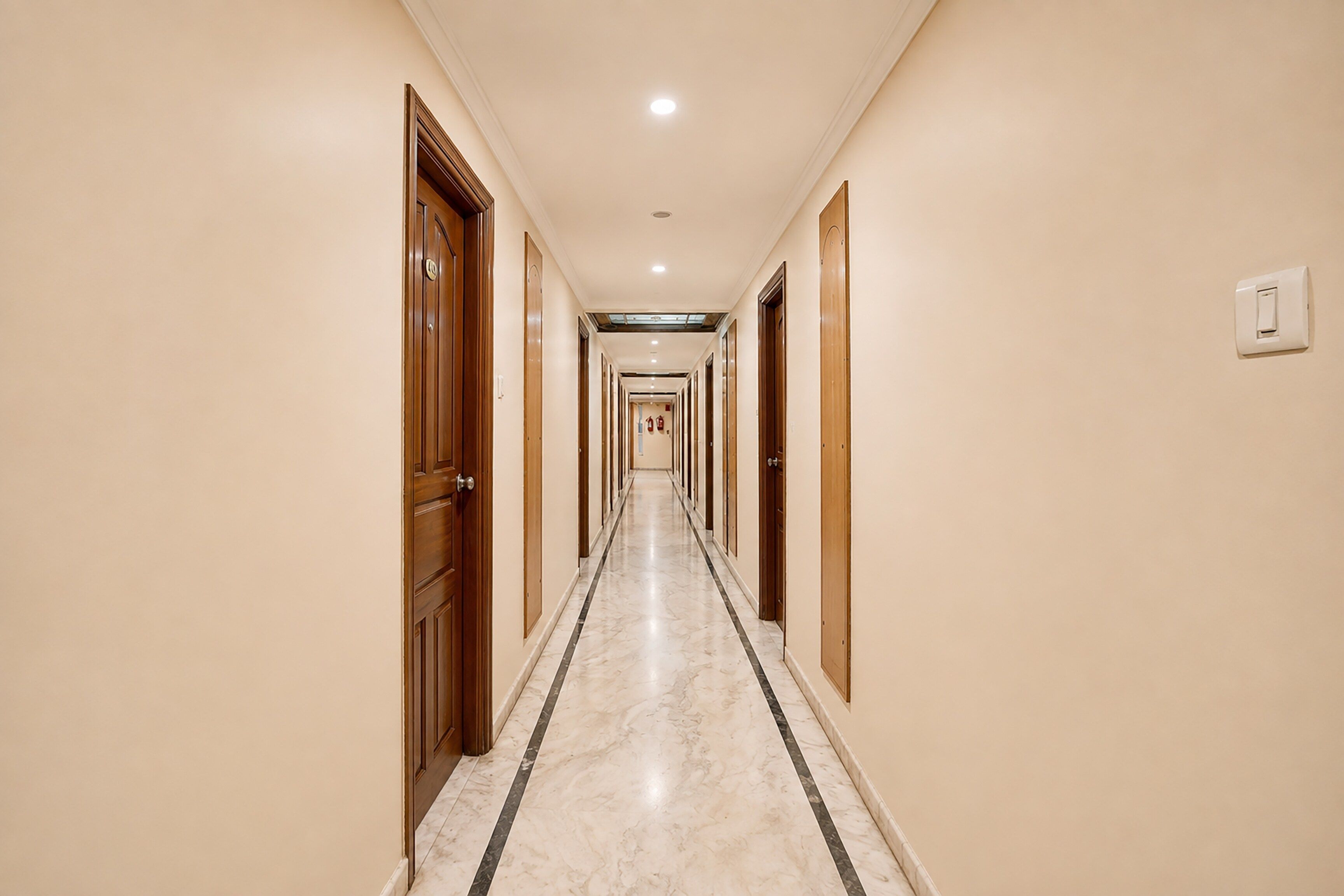 Un pasillo de hotel con puertas de madera, suelo de mármol y un interruptor de luz en la pared.