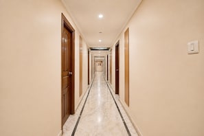 Un pasillo de hotel con puertas de madera, suelo de mármol y un interruptor de luz en la pared.