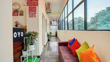 A hotel lobby with a reception desk, a clock, CCTV surveillance notice, and a sofa with colorful cushions.