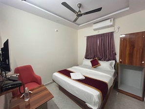 A hotel room with a bed, a desk with a computer and phone, a ceiling fan, an air conditioning unit, and a wardrobe. - Hotel O Srinidhi Inn (Bangalore)