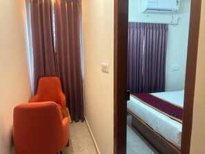 A hotel room with a bed, a chair, and an air conditioning unit. - Hotel O Srinidhi Inn (Bangalore)