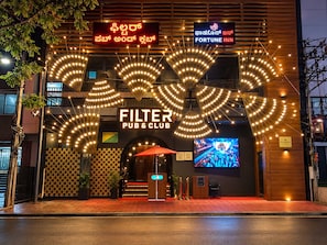 Un edificio con un llamativo letrero que dice 'FILTER PUB & CLUB', un letrero 'FORTUNE INN' y una pantalla grande mostrando un evento.