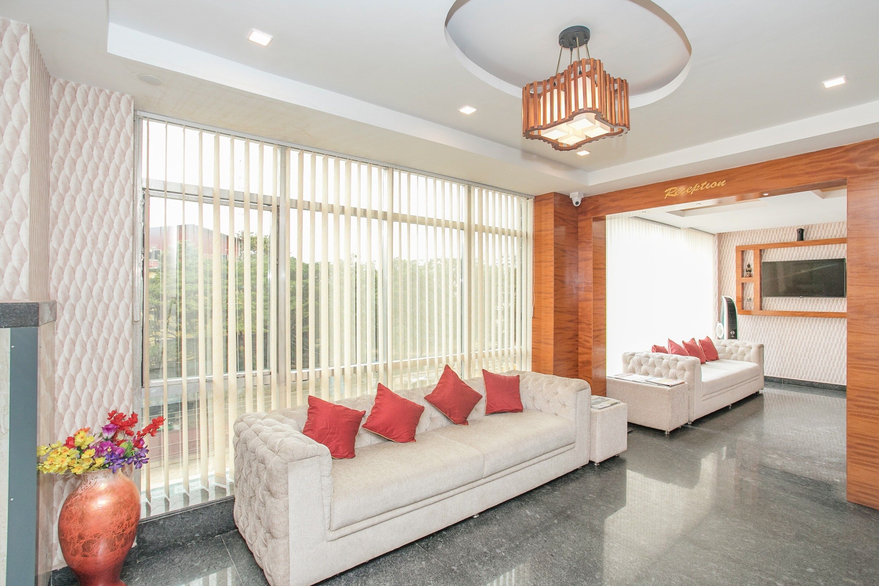 A hotel lobby with a reception desk, a sofa with red cushions, and a large window with blinds.