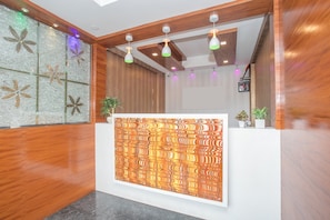 Zona de recepción con un mostrador de madera, pared con diseño y luminarias en el techo.