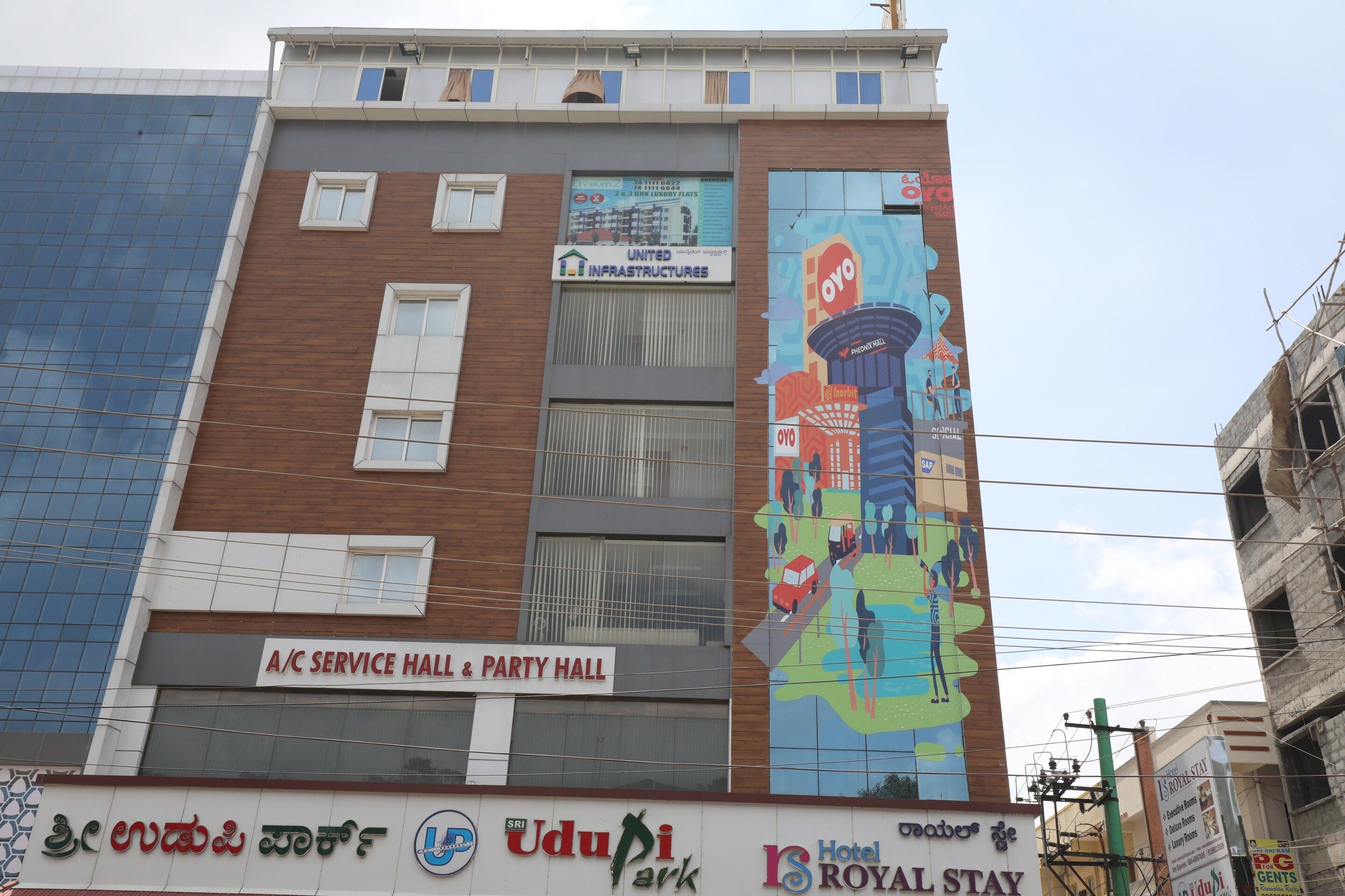 A building with a service hall and party hall on the ground floor, a mural on the side, and multiple signs for businesses including a hotel.