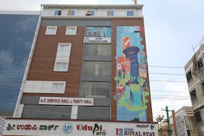 Un edificio con salón de servicios y salón de fiestas en la planta baja, un mural lateral y varios letreros de comercios, incluyendo un hotel.