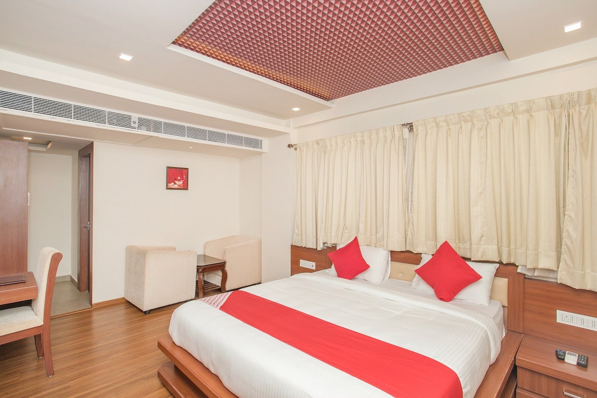 Habitació d'hotel amb llit, escriptori, cadira i finestra amb cortines.