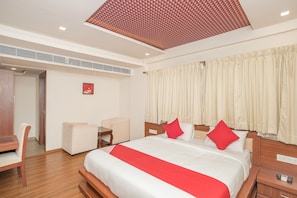Habitació d'hotel amb llit, escriptori, cadira i finestra amb cortines.