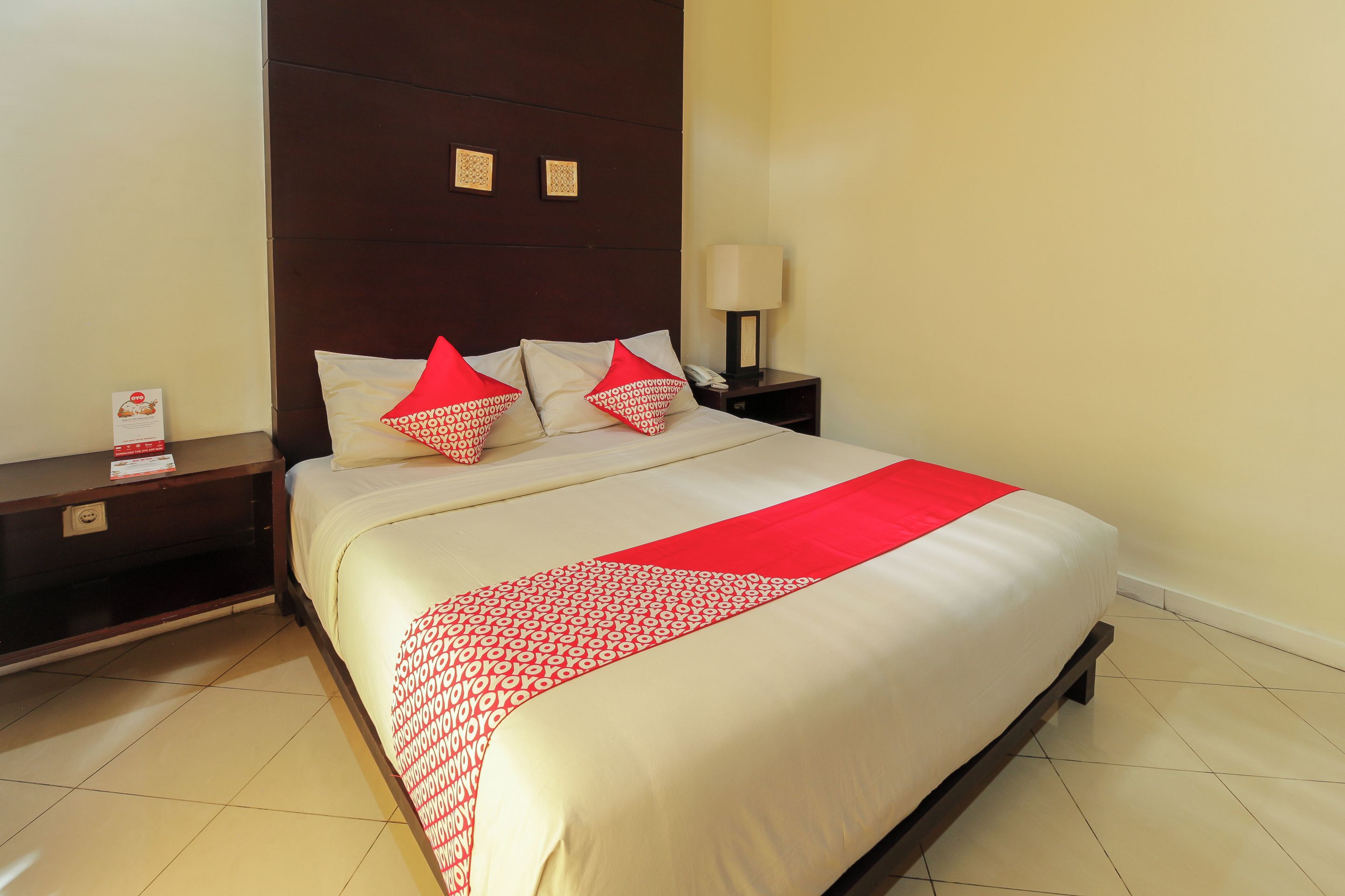 Habitación de hotel con una cama grande, una mesita de noche con lámpara y un teléfono instalado en la pared.