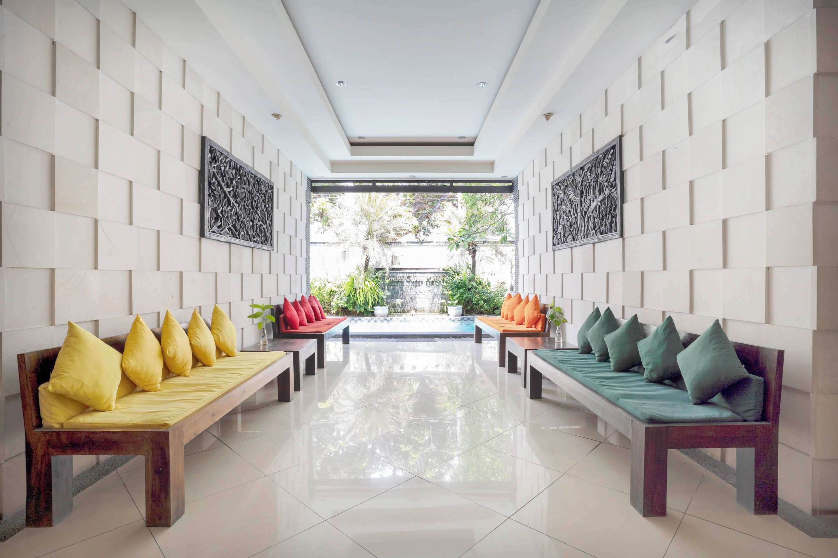 A modern lobby with two wooden benches, each with cushions, flanking a central walkway.