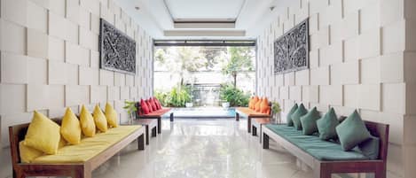 A modern lobby with two wooden benches, each with cushions, flanking a central walkway.