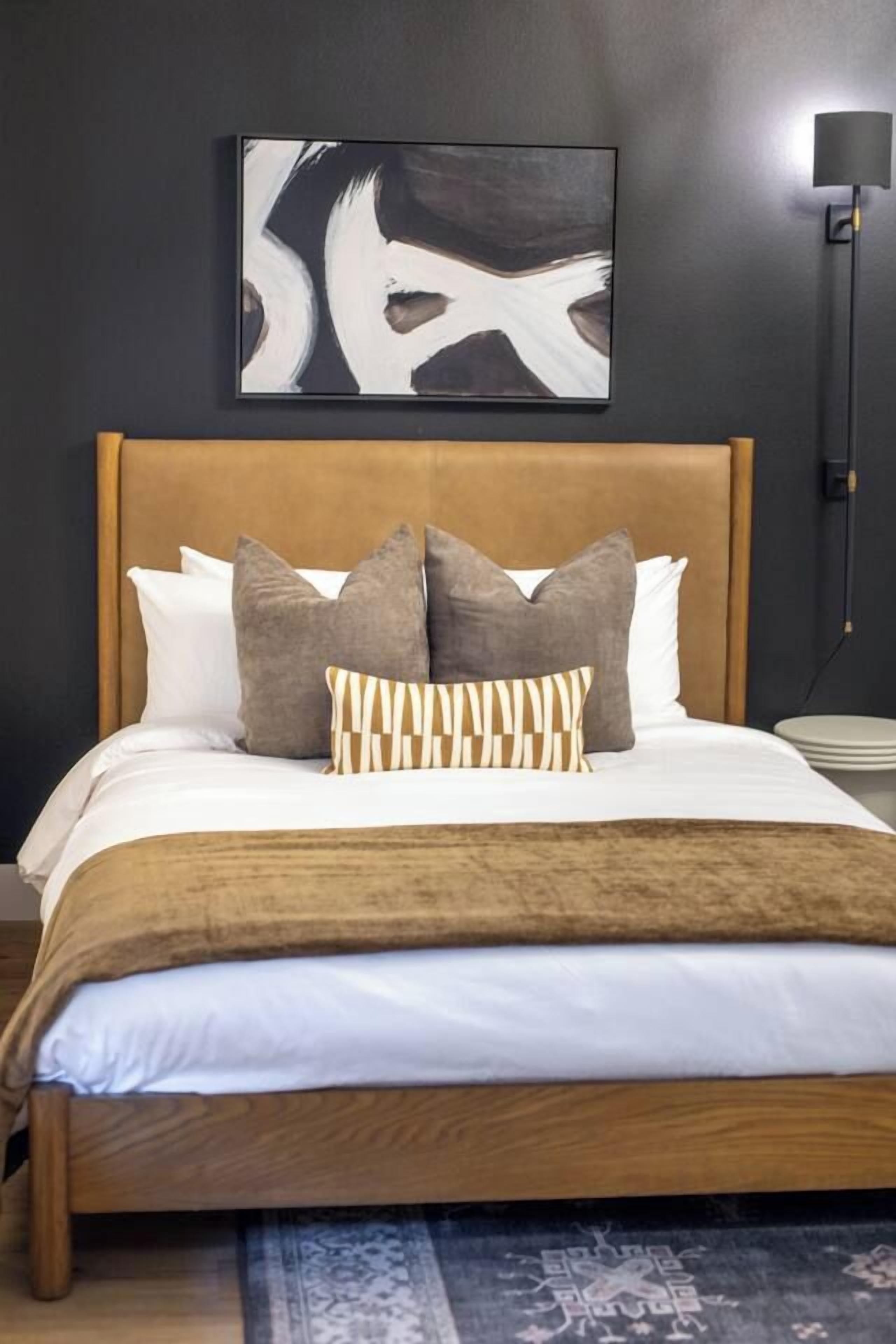 Un lit avec une tête de lit en bois, plusieurs oreillers et un plaid à motifs.