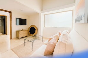 Ein modernes Wohnzimmer mit einer Couch, einem Glastisch, einem Fernseher und einem großen Fenster.