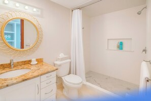 Ein Badezimmer mit Marmorwaschbecken, Toilette, Dusche und einem beleuchteten Spiegel.