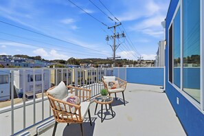Un balcon avec deux fauteuils en osier et une petite table, donnant sur un quartier résidentiel avec des maisons et des lignes électriques.