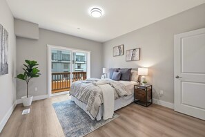 Une chambre à coucher avec un lit, des tables de chevet, une plante en pot, une fenêtre donnant sur un beau paysage et une porte.