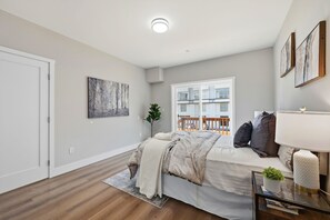 Ein Schlafzimmer mit Bett, Fenster, Pflanze und Bildern an der Wand.