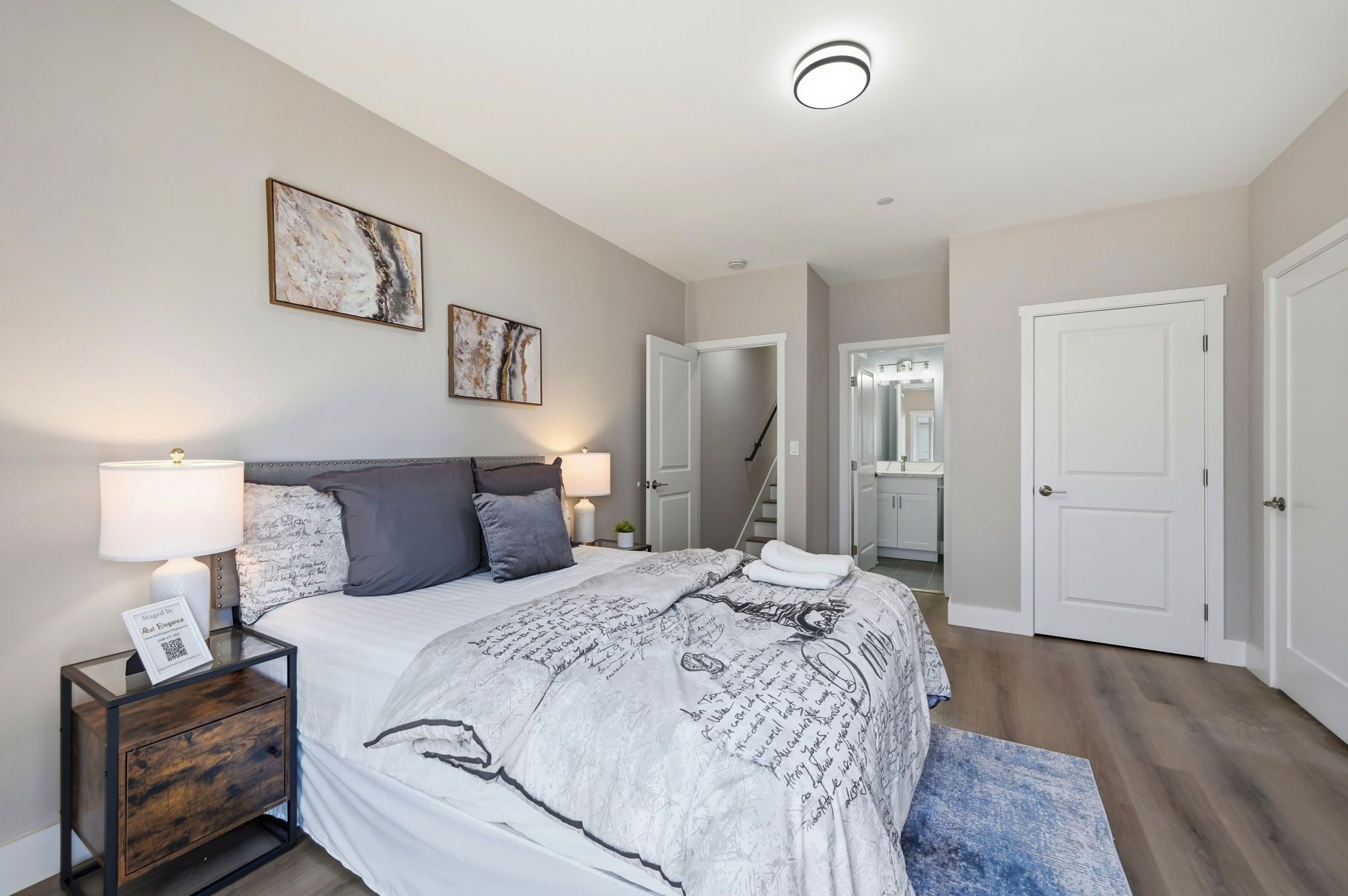 Une chambre à coucher comprenant un lit, des tables de chevet, une lampe, un tapis et une porte donnant sur une salle de bain.