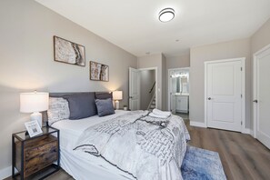 Une chambre à coucher comprenant un lit, des tables de chevet, une lampe, un tapis et une porte donnant sur une salle de bain.