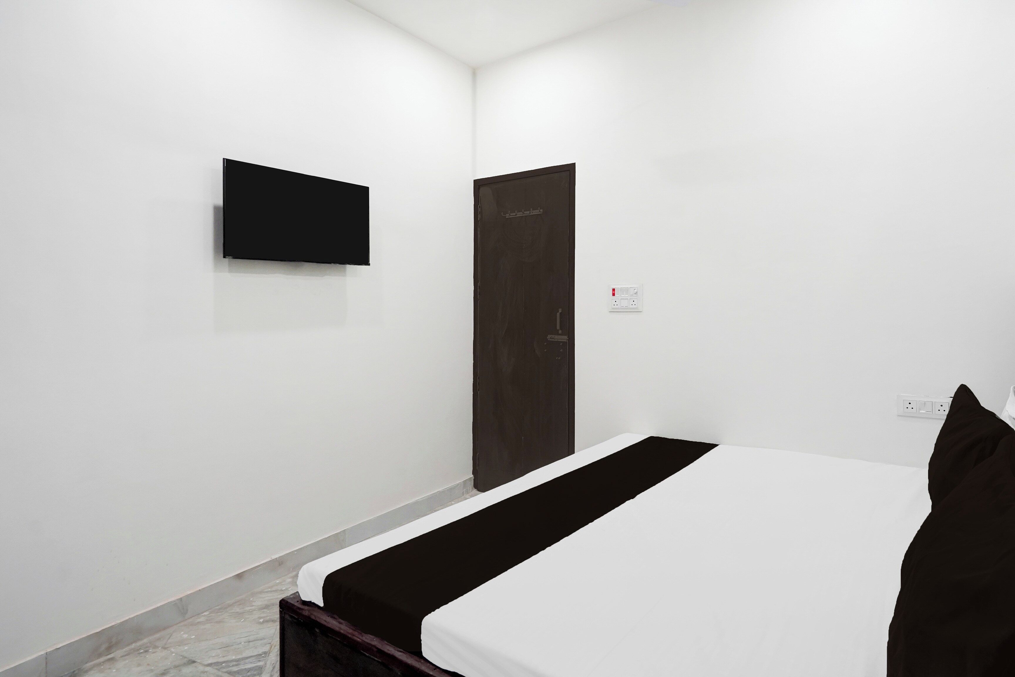 A hotel room with a bed, a television mounted on the wall, a door, and a power outlet.