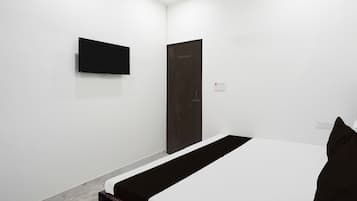 A hotel room with a bed, a television mounted on the wall, a door, and a power outlet.