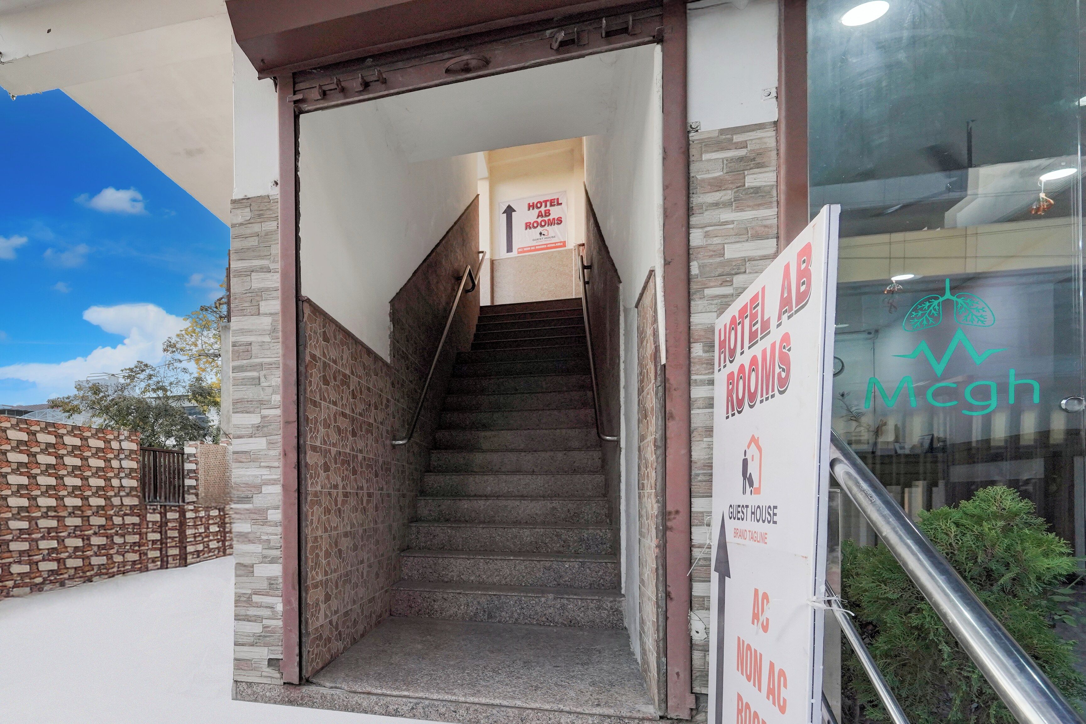 A hotel entrance with a staircase leading to the rooms, a sign indicating guest house, and a logo for Mcgh.