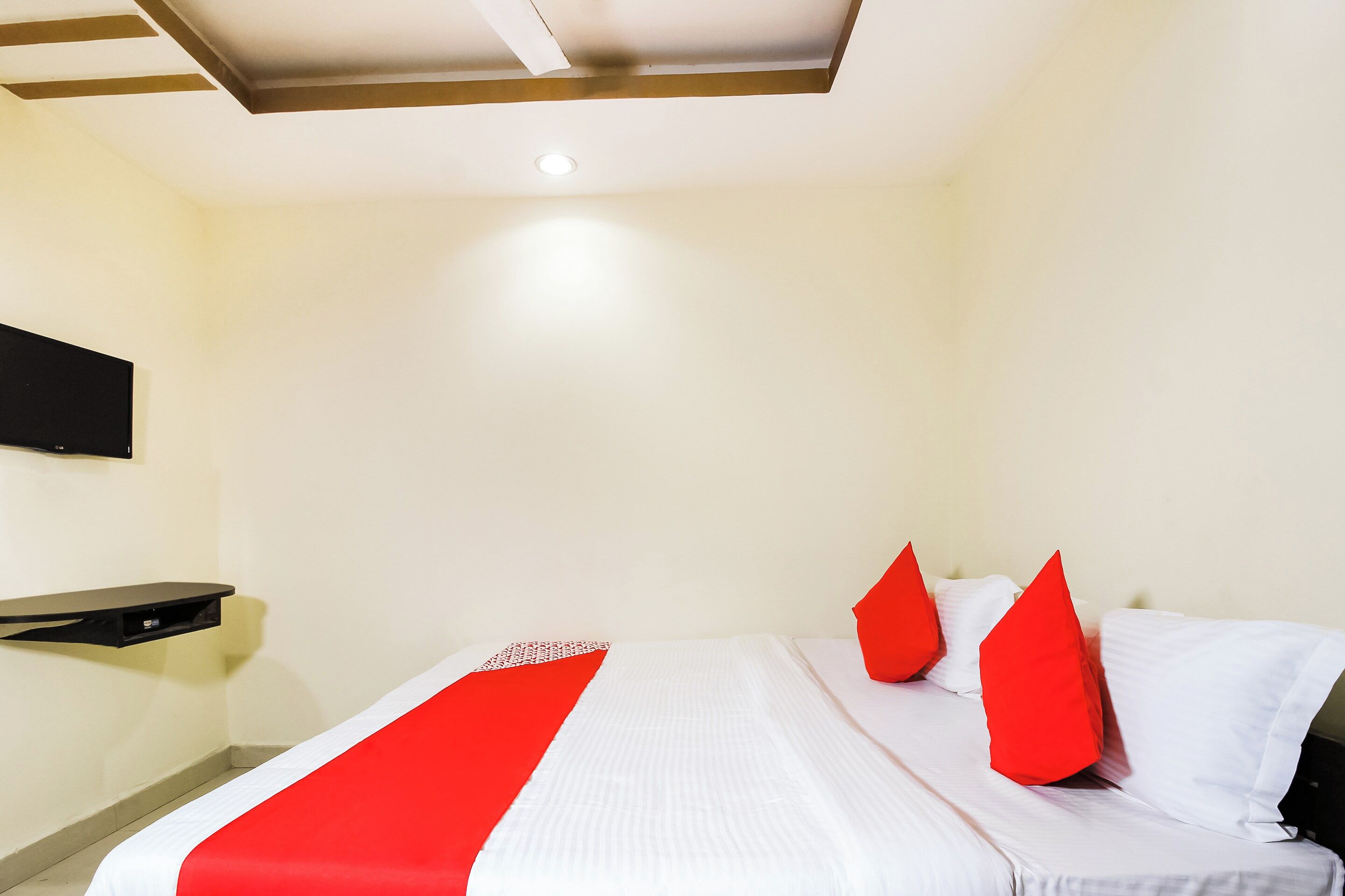 A hotel room with a bed, pillows, and a flat-screen TV mounted on the wall.