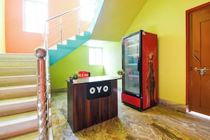 Una recepción con un letrero, una escalera, un refrigerador y una puerta.