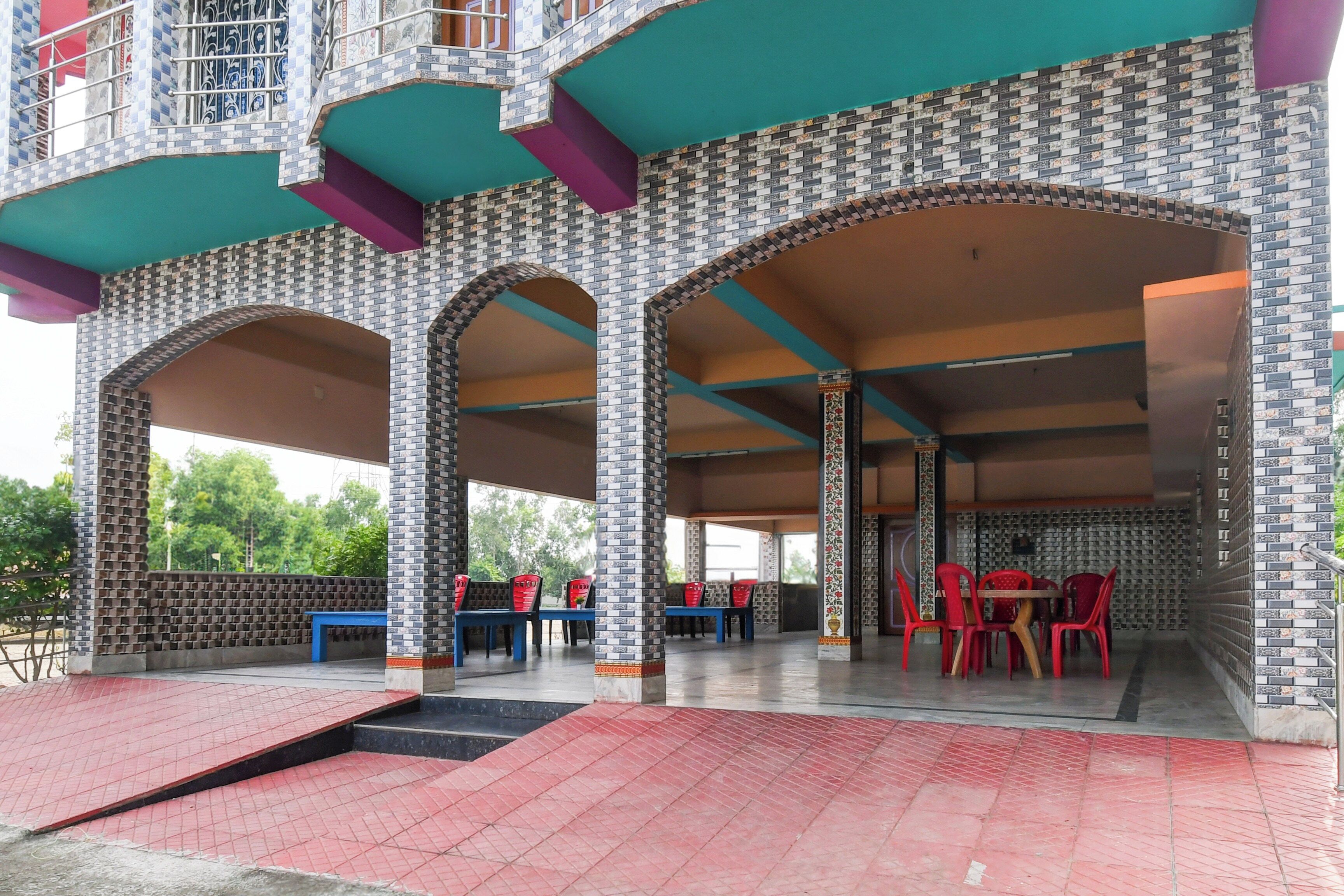 Un espacio de estar al aire libre con techo, con sillas y mesas rojas, rodeado por un muro con diseño y una escalera que sube a un balcón.