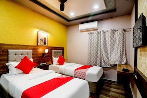 A hotel room with two beds, a ceiling fan, an air conditioning unit, a TV, and a patterned curtain. - Hotel O Padma Manor (Behrampur)
